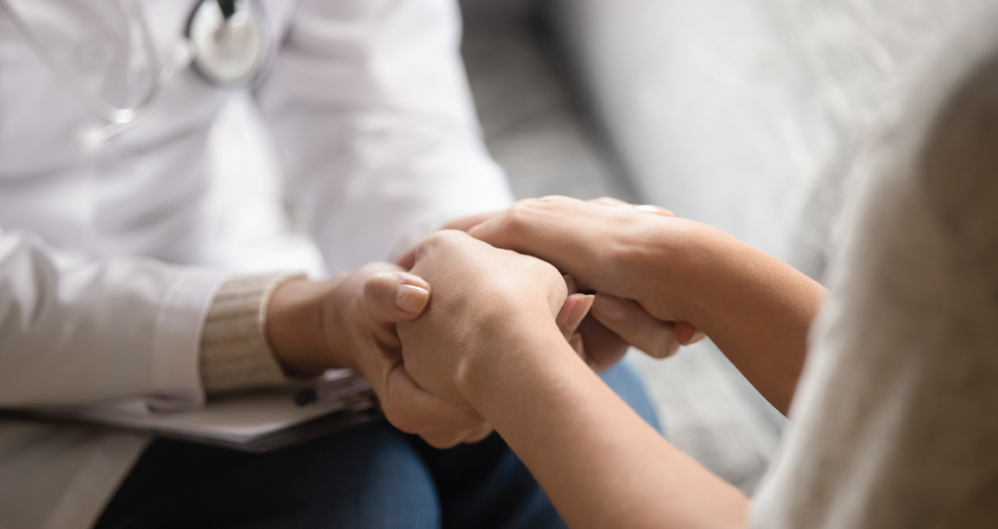 Doctor holds hands with patient providing comfort.